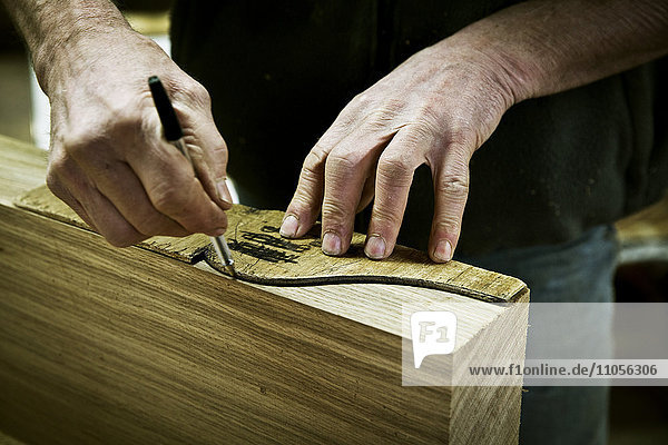 Ein Mann  der in der Werkstatt eines Möbelherstellers arbeitet und eine Form auf Holz zeichnet.