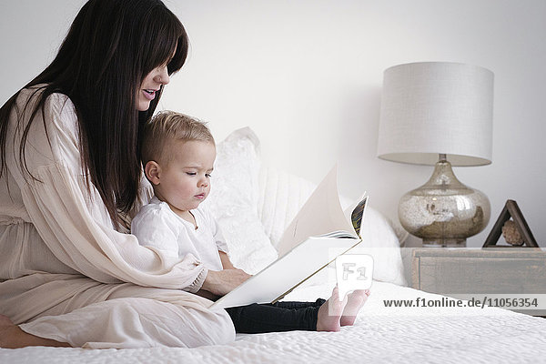 A heavily pregnant woman playing with her young son. Sitting on a bed  reading a story.