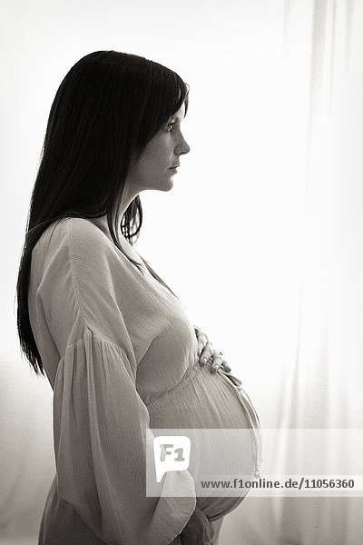 Eine hochschwangere Frau mit den Händen auf dem Bauch im Profil gesehen.
