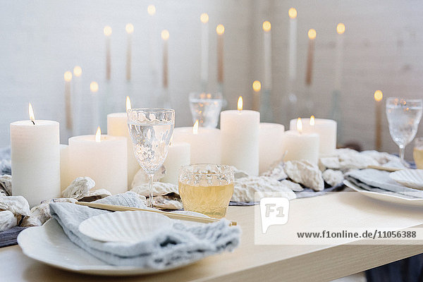 Ein Tisch mit brennenden Kerzen  Porzellantellern und Gläsern.