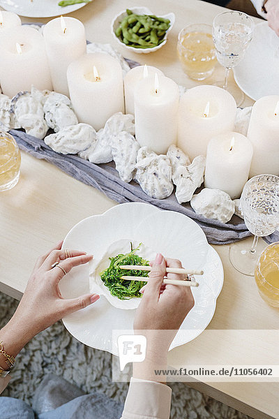 Draufsicht auf einen Tisch mit Kerzen und eine Person  die mit Stäbchen grünes Gemüse isst.