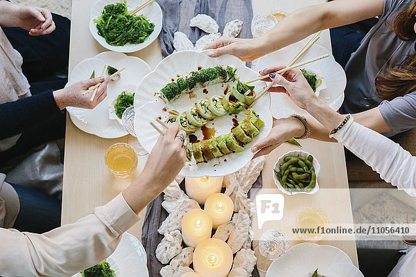 Overhead view of four people sharing a meal  plates of sushi and a table setting for a celebration meal.