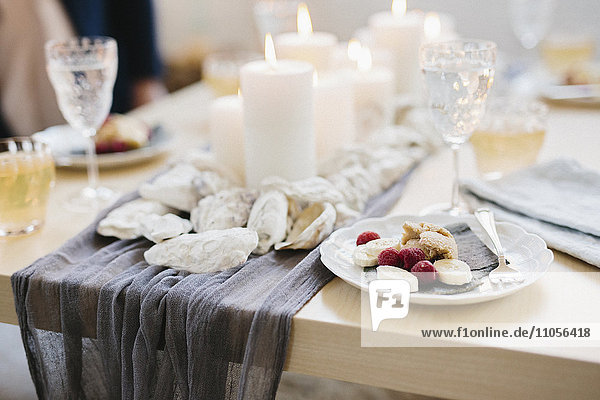 Ein Tisch für ein Festmahl mit gefüllten Weingläsern und Obsttellern und angezündeten Kerzen in der Mitte des Tisches.