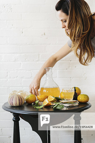 Eine Frau arrangiert geschnittene Orangen auf einem Tisch neben einem hohen Krug mit Saft.