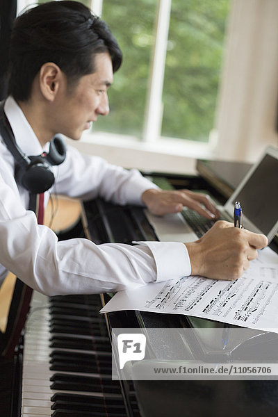 Young man sitting at a grand piano in a rehearsal studio  annotating sheet music.