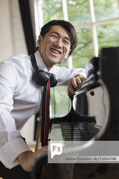 Young smiling man sitting at a grand piano in a rehearsal studio  wearing headphones round his neck.