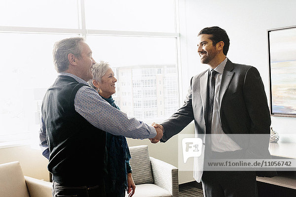 A man greeting a mature couple in an office.