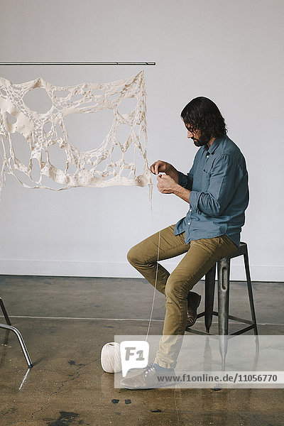 Ein Künstler  der an einem Kunstwerk arbeitet und ein gewebtes und genähtes Objekt mit Faden herstellt.