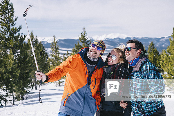 Drei Personen  zwei Männer und eine junge Frau in Skiausrüstung  posieren für einen Selfie  einer hält einen Selfie-Stock.