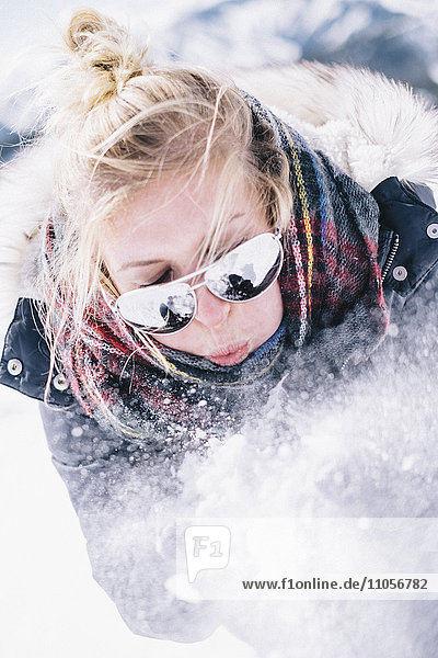 Eine junge Frau mit Sonnenbrille bläst sich frischen Schnee von den Händen.