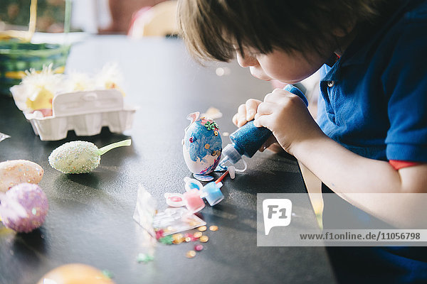 Ein Kind schmückt zu Ostern Eier mit Glitzer,  Kleber und Farbe.