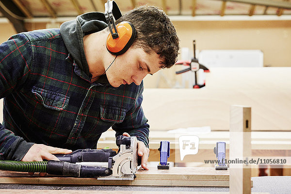 Eine Möbelwerkstatt  die maßgeschneiderte zeitgenössische Möbelstücke unter Verwendung traditioneller Fertigkeiten im modernen Design herstellt. Ein junger Mann benutzt Werkzeuge  um ein Stück Holz zu formen.