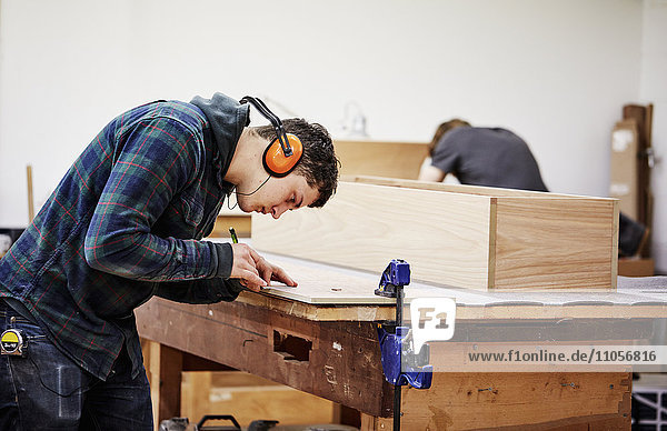 Eine Möbelwerkstatt  die maßgeschneiderte zeitgenössische Möbelstücke unter Verwendung traditioneller Fertigkeiten im modernen Design herstellt. Ein Mann markiert ein Stück Holz mit einem Bleistift.