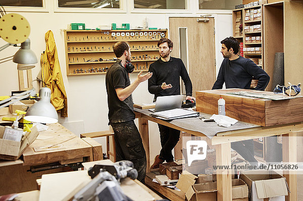 Eine Möbelwerkstatt  die maßgeschneiderte zeitgenössische Möbelstücke unter Verwendung traditioneller Fertigkeiten im modernen Design herstellt. Drei Personen an einem Tisch  die einen Plan besprechen.
