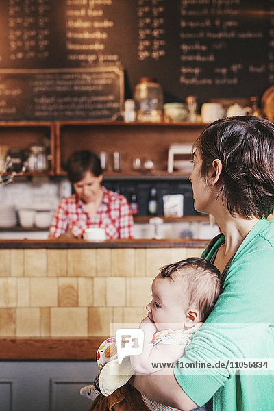 Zwei Frauen  ein gleichgeschlechtliches Paar mit ihrem 6 Monate alten Baby in ihrem Café. Geschäftsinhaber und Eltern.