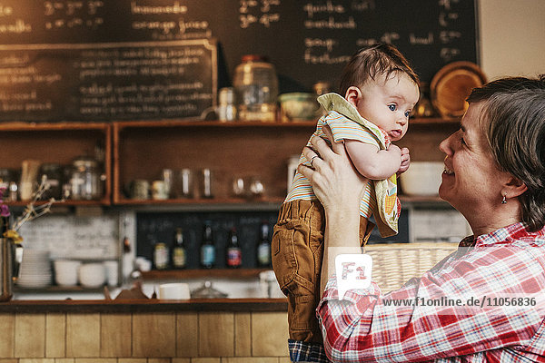A woman holding up a young baby at a coffee shop.