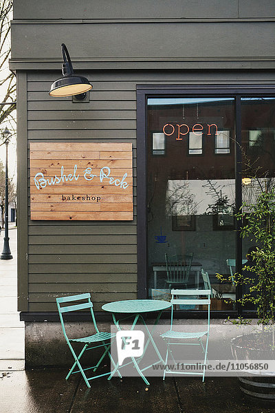 Das Äußere eines kleinen Geschäfts Straßenansicht eines Cafés mit Tisch und Stühlen im Freien.
