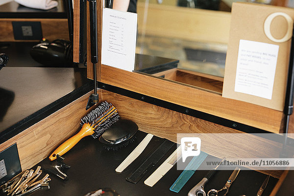 A workstation with hair combs  scissors and hair pins laid out neatly in front of a mirror.