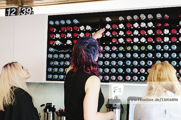 A woman reaching up to select a ground coffee pod to use to maker a morning coffee in the kitchen of the hair salon.