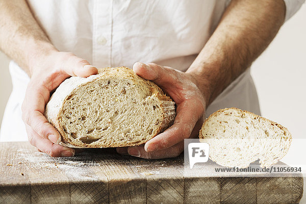 Bäcker hält einen frisch gebackenen Laib Brot in der Hand.