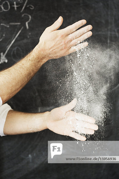 Nahaufnahme eines Bäckers  der vor einer Tafel steht und seine Hände mit Mehl bestäubt.