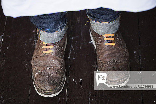 Nahaufnahme der Füße eines Mannes  der braune Schuhe mit orangefarbenen Schnürsenkeln trägt.