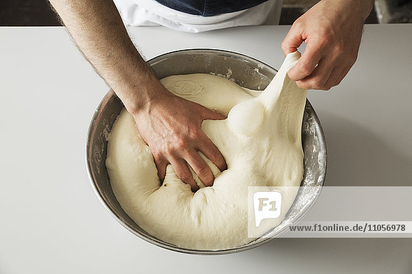 Nahaufnahme eines Bäckers  der Brotteig in einer Metallschüssel knetet.