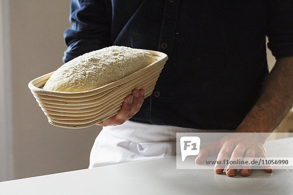 Nahaufnahme eines Bäckers  der einen frisch gebackenen Laib Weißbrot in einem Gärkorb aus Rattan hält.