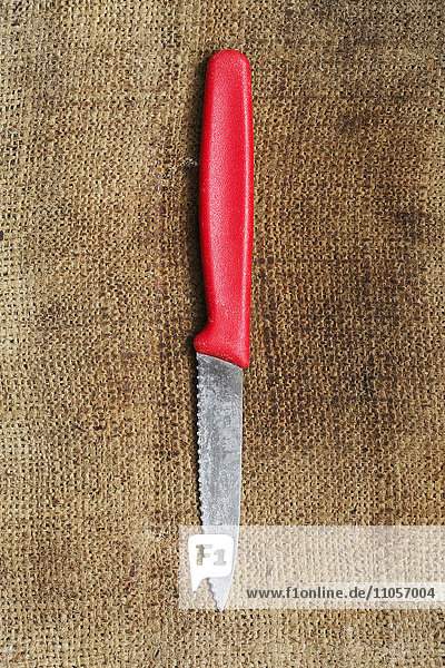 Nahaufnahme eines Küchenmessers mit rotem Plastikgriff auf Sackleinen.