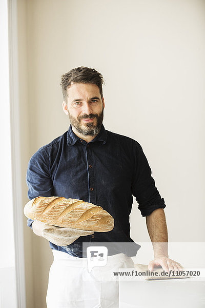 Bäcker hält zwei frisch gebackene Brotlaibe in der Hand.