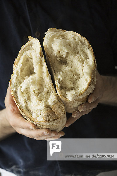 Nahaufnahme eines Bäckers  der einen frisch gebackenen  in zwei Hälften gerissenen Weißbrotlaib in der Hand hält.