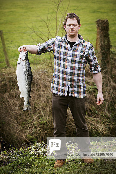 A man standing holding a large freshly caught salmon fish.