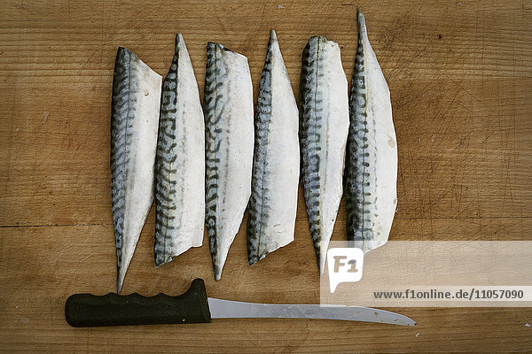 Fresh Mackerel fillets and a knife on a chopping board.