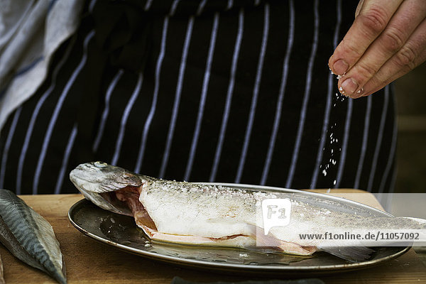 Close up of a chef sprinkling salt onto a fresh fish.