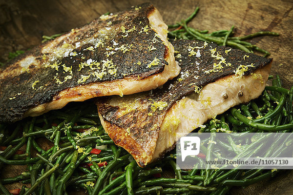 Close up of grilled fish fillets with crispy skin on a bed of samphire.