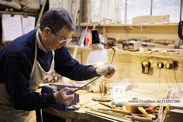 Man standing at a work bench in a carpentry workshop  working on a piece of wood secured in a bench vice.