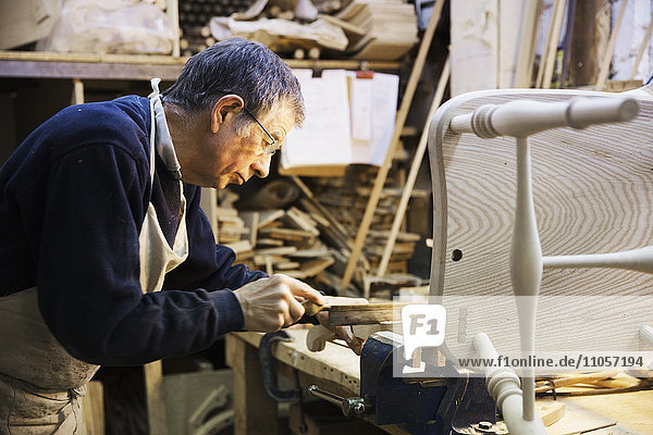 Man standing at a work bench in a carpentry workshop  working on a wooden chair.