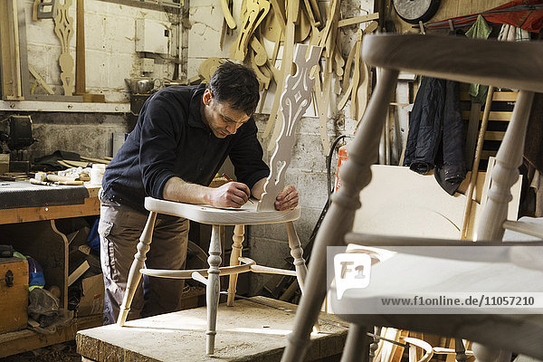 Man standing in a carpentry workshop  working on a wooden chair.