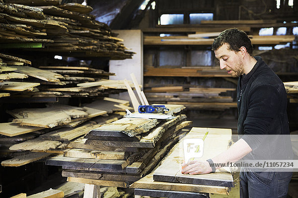 Mann  der in einer Schreinerei arbeitet und ein Brett aus Holz vermessen hat.