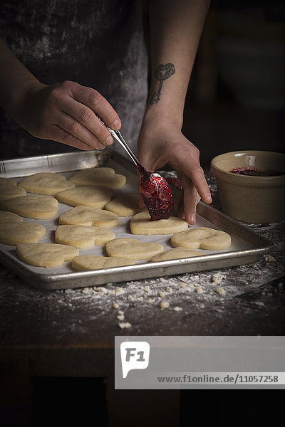 Valentinstag beim Backen  Frau streicht Himbeermarmelade auf herzförmige Kekse.