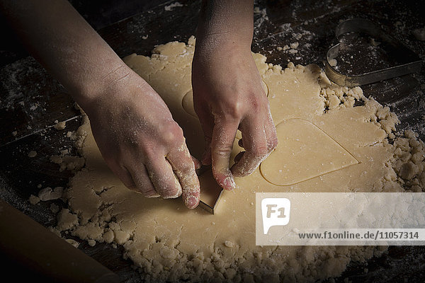 Valentinstag backen  Frau schneidet aus dem Teig herzförmige Kekse aus.