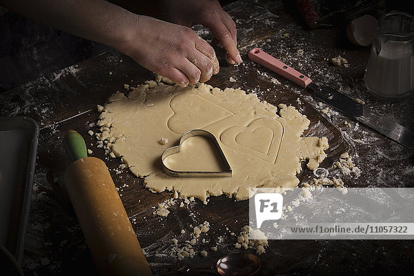 Backen zum Valentinstag. Frau schneidet auf einer bemehlten Fläche herzförmige Kekse aus Teig aus.