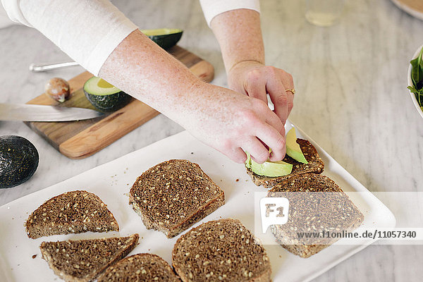 Eine Frau bereitet ein Sandwich mit Schwarzbrotscheiben und Avocadoscheiben zu.