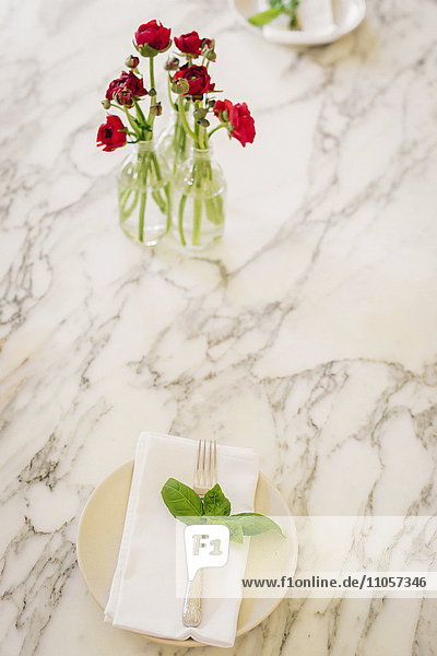Eine Marmortischplatte und eine Vase mit frischen roten Schnittblumen und Serviette mit Kräuterbasilikum.