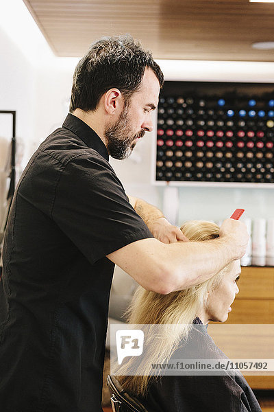 Ein reifer Mann  ein Hairstylist  Colorist  der am Haar einer Frau arbeitet und Haarfarbe auf den Mittelscheitel aufträgt.