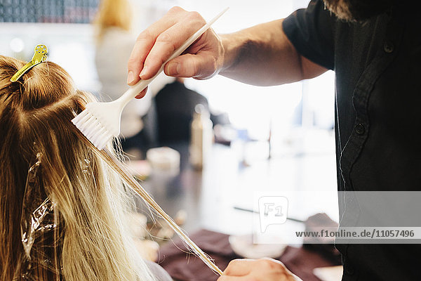 A hair colourist  a man using a paintbrush to cover sections of a woman's blonde hair.