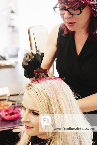 Ein Haarkolorist mit Handschuhen  der mit einer Bürste rote Haarfarbe auf das blonde Haar eines Kunden aufträgt.