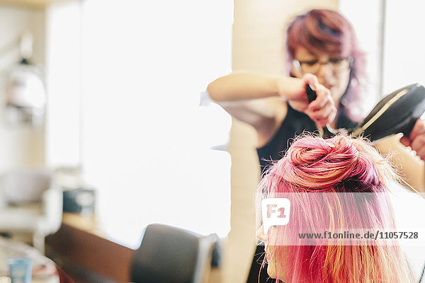 A hair stylist blow-drying a client's long pink dyed hair.