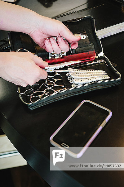 Ein Friseursalontisch  ein Smartphone und eine Frauenhand  die in einen Beutel für Friseurscheren und -klammern greift.
