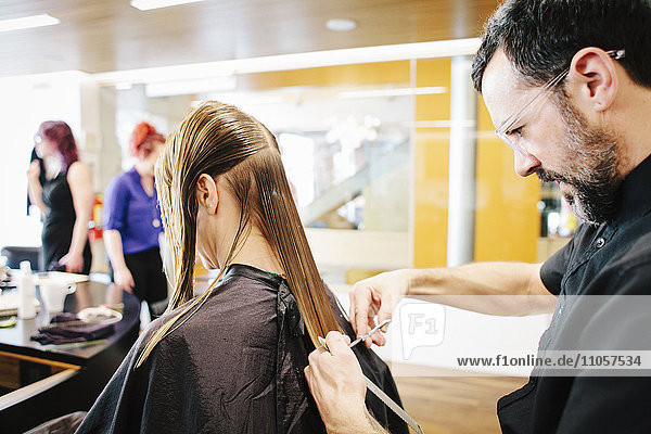 A hair stylist with a client  cutting her long straight hair.